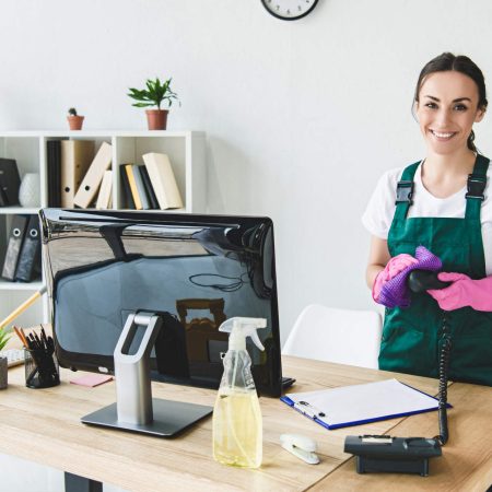 Professional office cleaning service showing cleaner with spray bottle and another cleaner holding cleaning tools at a modern office desk